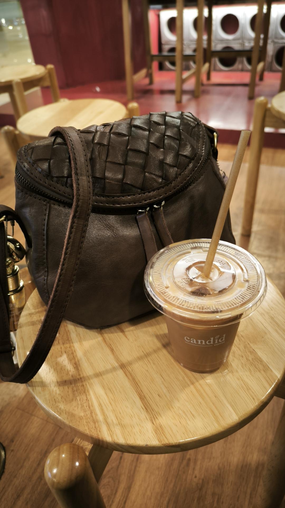 brown leather bag with a woven pattern beside a plastic coffee cup from candid coffee