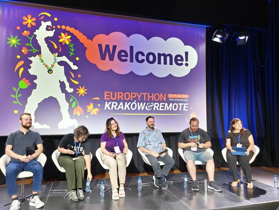 Six people in chairs in front of the purple EuroPython slide that features a stylized dragon saying "Welcome!"