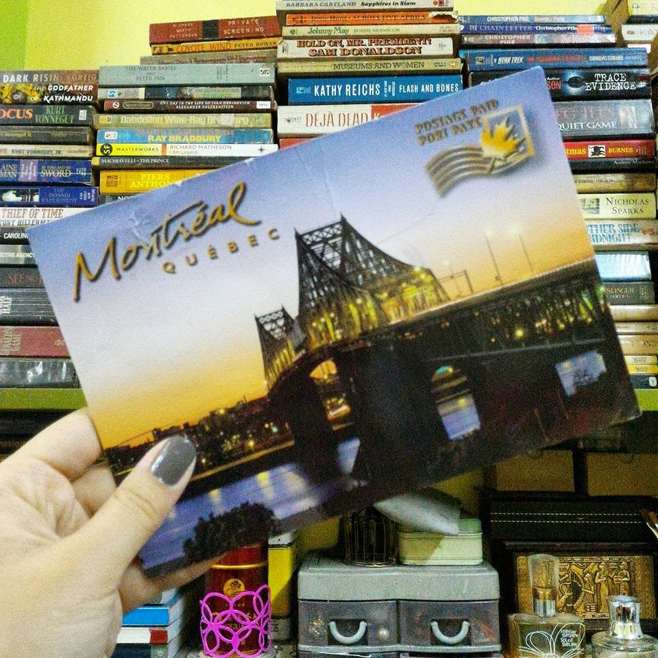 a hand holding up a montreal postcard with a stack of books and other items behind