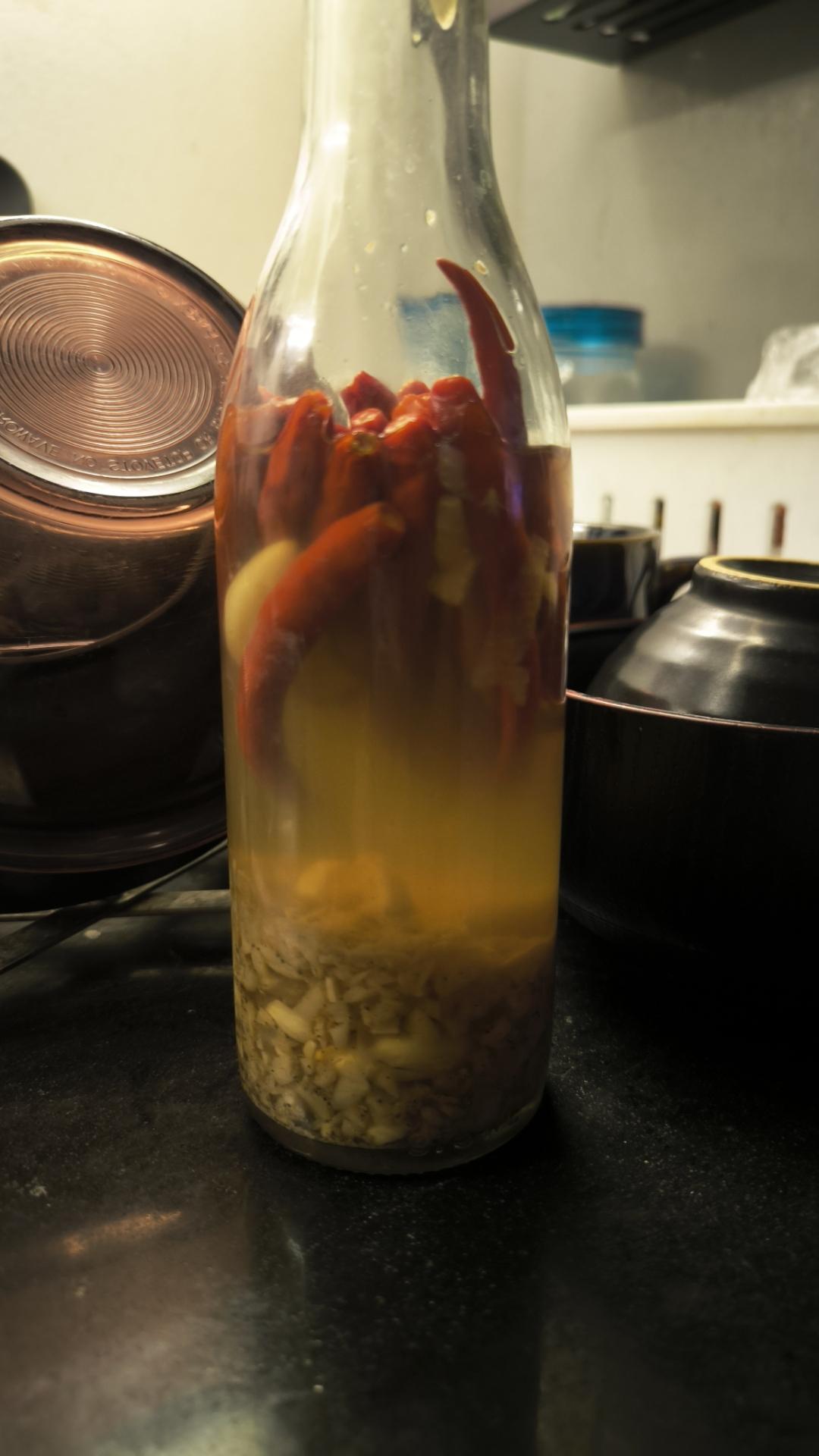clear bottle of vinegar also containing garlic and whole chilis