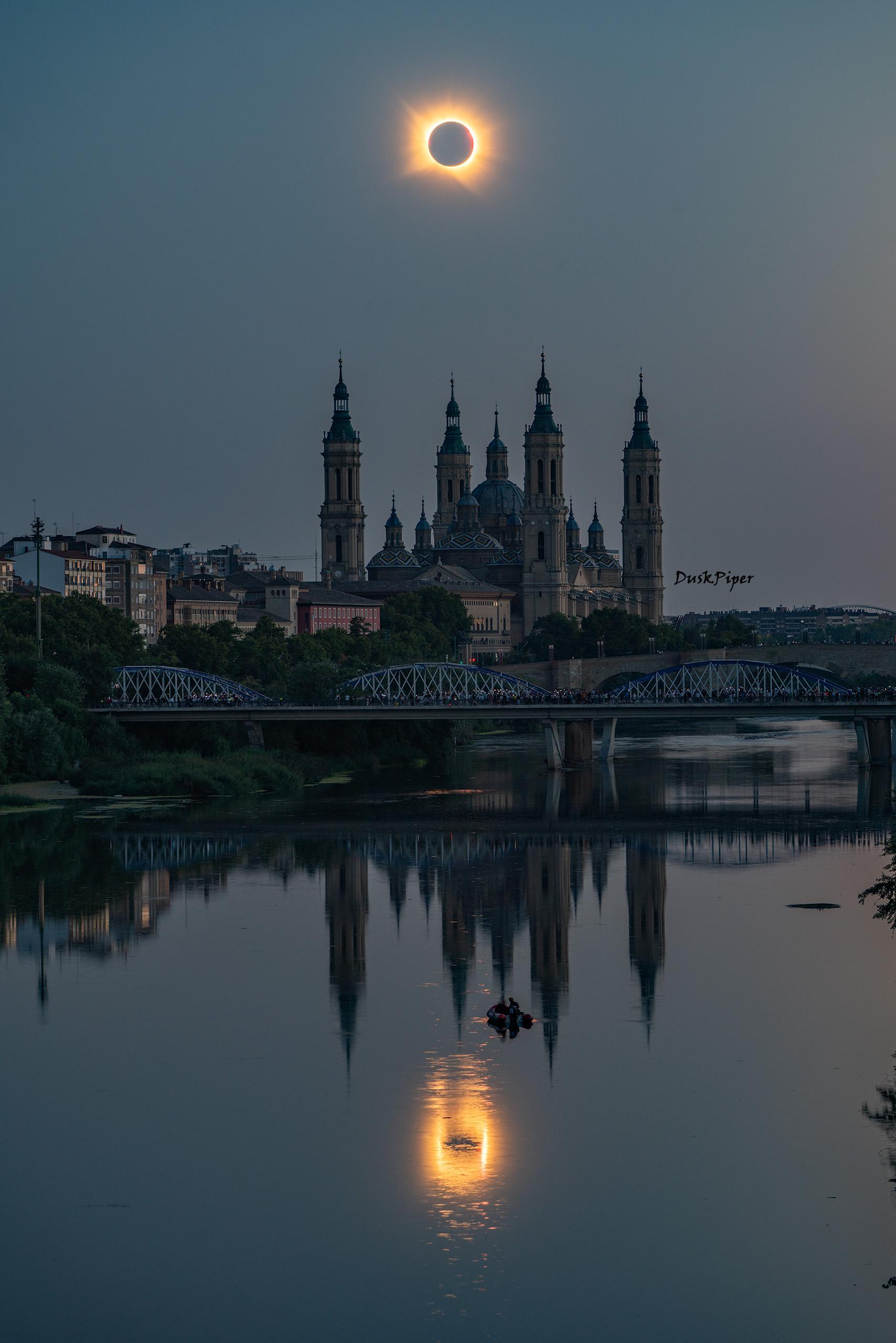 On August 12th, 2026, the Moon totally eclipsed the Sun and cast its shadow across Siberia, Greenland, Iceland, Spain, and Portugal. Today’s image features two total solar eclipses viewed from Zaragoza, Spain, one over the Cathedral-Basilica of Our Lady of the Pillar and the other reflecting in the Ebro River. For a few moments, Spain saw its first major total solar eclipse since 1905. Those witnessing totality may experience a chill in the air, the quieting of birds, the confused chirps of insects, and the shared awe of many. It’s the corona’s time to shine as the Sun’s bright disk is blocked by the Moon. Among other reasons to study eclipses, they help scientists understand why the corona is millions of degrees hotter than the Sun’s surface. Enthusiastic citizens can contribute to these studies by recording how wildlife responds, imaging the corona, and monitoring air temperature and clouds.